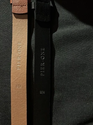 Två skärp från Pier One i skinn - Säljer två klassiska skärp från Pier One, ett i brunt och ett i svart skinn. Båda har stilrena silverfärgade metallspännen och enkel design som passar till många olika outfits. Perfekta accessoarer för att lyfta din look.