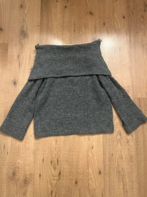 Grå off shoulder stickad tröja H&M - Mysig grå stickad tröja från H&M med off shoulder-design och långa ärmar. Tröjan har en bred krage som viks ner över axlarna och är tillverkad i ett mjukt, ribbstickat material. Perfekt för en avslappnad och trendig look. Stor i storleken.