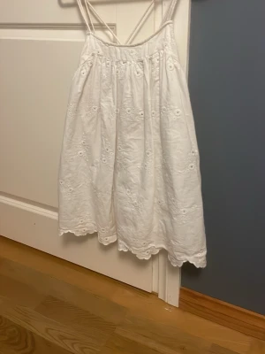Vit somrig klänning/ byxklännig - Söt vit kortklänning med tunna axelband och broderade blommor. Har även shorts insydda och fickor. Från Zara.