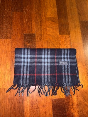 Mörkblå halsduk från burberrys - Säljer denna väldigt snygga burberry halsduken. 100% lammull och är perfekt nu när det är extra kallt. Funkar för tjejer och killar.