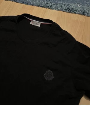 Svart t-shirt från Moncler - Snygg svart t-shirt från Moncler med diskret logga på bröstet. Klassisk rund halsringning och korta ärmar. Perfekt till jeans eller shorts för en clean och stilren look.