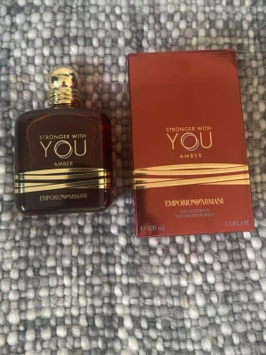 Emporio Armani Stronger With You Amber - Emporio Armani Stronger With You Amber är en lyxig parfym i en elegant mörk bärnstensfärgad glasflaska med gulddetaljer och rund guldfärgad kork. Flaskan rymmer 100 ml och doften har en varm, orientalisk karaktär. Helt ny kostar 1000kr+