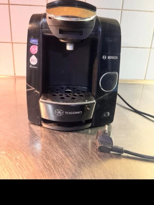 Svart kaffemaskin Bosch Tassimo - Säljer en svart kaffemaskin från Bosch, modell Tassimo. Maskinen har en rundad form och är tillverkad i plast med silverfärgade detaljer. Perfekt för att brygga kaffe med kapslar. Enkel att använda med knapp på framsidan.