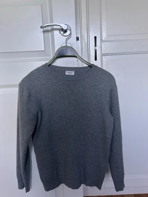 Grå stickad tröja från KappAhl - En enkel och stilren grå stickad tröja från KappAhl med rund halsringning och långa ärmar. Tröjan har ribbstickade muddar vid ärmslut och nederkant, perfekt för lager-på-lager och en clean look. PRISET KAN DISKUTERAS VID SNABB AFFÄR!