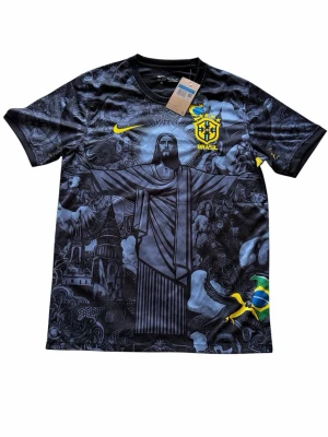 Brazil fotbolls jersey - Säljer en svart Nike fotbollströja för Brasilien med unikt tryck av Kristusstatyn och brasilianska motiv. Tröjan har gula detaljer, Brasilien-emblem och Nike-logga. Tillverkad i Dri-FIT-material som andas, perfekt för träning eller match. Har aldrig använts 
