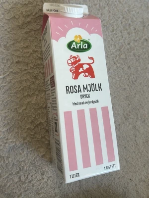 Arla rosa mjölkdryck jordgubb 1L - En 1 liters förpackning rosa mjölkdryck från Arla med smak av jordgubb. Kartongen är vit och rosa med illustration av en ko och jordgubbar. Perfekt till att dricka som den är eller använda i recept som mannagrynsgröt. Den är tom 