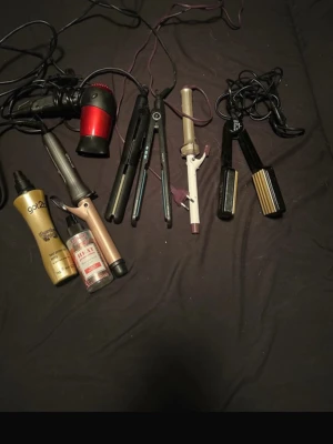 Paket med hårstylingverktyg & produkter - Säljer ett paket med flera hårstylingverktyg: hårfön i rött och svart, två plattänger, två locktänger (en beige/rosa och en vit), en vågtång samt två stylingprodukter från got2b och Syoss. Perfekt för dig som gillar att styla håret på olika sätt. Allt för 250kr