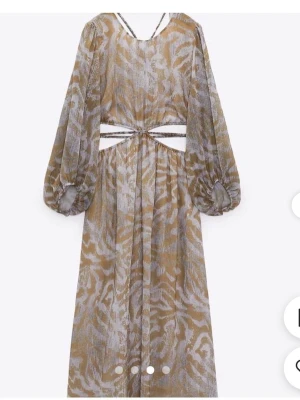 Zara Långklänning med zebra-mönster och öppen rygg - Trendig långklänning med beige och vita zebraränder, ballongärmar och coola cut-outs i midjan. Klänningen har öppen rygg med snygga banddetaljer. Från zara som ny. 