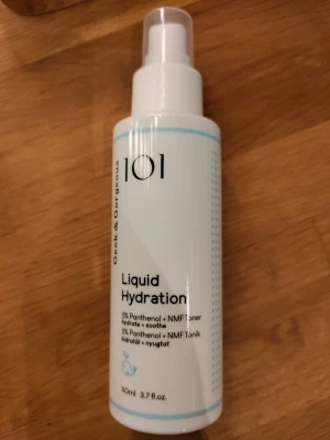 Geek & Gorgeous Liquid Hydration Toner - En genomskinlig toner i sprayflaska från Geek & Gorgeous, Liquid Hydration med 5% panthenol och NMF. Flaskan är vit med blå detaljer och rymmer 110 ml. Perfekt för att återfukta och lugna huden med en lätt, silkeslen känsla.