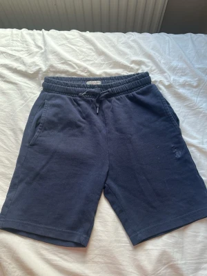 Blå shorts från Polo Ralph Lauren - Mörkblå shorts från Polo Ralph Lauren med broderad logga på benet. Sköna shorts i bomull med resår och snörning i midjan samt två sidofickor. Perfekta för sommaren och chill dagar. För barn som är mellan     9-10 år.