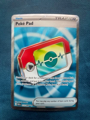 Pokémonkort Poké Pad Trainer full art - Pokémonkort Poké Pad Trainer Item med färgglad design i rött, vitt, grönt och blått. Kortet har en digital Pokédex-illustration och text på engelska. Perfekt för samlare eller Pokémon TCG-spelare som vill utöka sin kortlek.