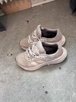 Beige Adidas sneakers med mesh - Snygga beige sneakers från Adidas med klassiska ränder på sidan. Ovandelen är i meshmaterial för bra andningsförmåga och skon har en tjock, bekväm sula. Perfekta för en sportig och avslappnad stil.