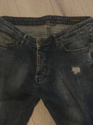 Mörkblå slim fit jeans från Hammond - Mörkblå slim fit jeans från Hammond med slitna detaljer och patch på höger lår. Klassisk femficksmodell med dragkedjegylf och knapp. Jeansen har en tvättad look och är tillverkade i denim.