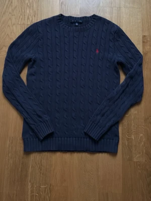 Mörkblå kabelstickad tröja Polo Ralph Lauren - Kabelstickad mörkblå tröja från Polo Ralph Lauren med rund halsringning och långa ärmar. Marinblå tröja som matcher perfekt till ett par snygga jeans. Den är i bra skick och inga tecken på slitage. Strl S. Säljer för den har blivit för liten. Pris kan diskuteras. 