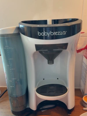 Baby Brezza PRO mjölkersättningsmaskin - Automatisk mjölkersättningsmaskin från Baby Brezza i vit och svart plast. Maskinen har en vattenbehållare på sidan med tydliga måttangivelser och en plats för nappflaska under utflödet. Perfekt för att snabbt blanda ersättning. Behövs ny pulverbehållare men annars inget konstigt! Äldre varianten. 