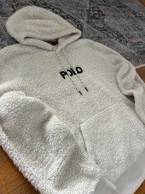 Ralph Lauren Pile Fleece Hoodie - Storlek M - Hej! 👋 Säljer en sjukt mysig och snygg vit Polo Ralph Lauren pile fleece hoodie i storlek M med mörkblå pony. 🐎✨ Tröjan är i gott skick och gjord i ett fantastiskt skönt material. Det finns en liten fläck på ena ärmslutet (se sista bilderna), men inget som stör helheten. 100% äkta med originaltvättlappar kvar och en fullt fungerande QR-kod för enkel verifiering ✅ Perfekt för sena kvällar eller tidiga morgnar! Fraktar snabbt! 💬 🚛📦 