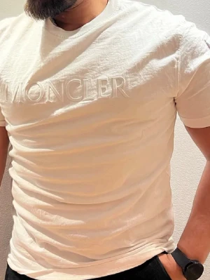 Vit Moncler t-shirt med broderad logga - Snygg vit t-shirt från Moncler med diskret broderad logotyp på bröstet. Klassisk passform och rund halsringning. Tillverkad i mjukt bomullsmaterial som känns skönt mot huden. Perfekt för en clean och stilren look.