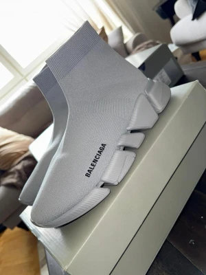 Grå Balenciaga Speed Trainer sneakers - Säljer ett par grå Balenciaga Speed Trainer sneakers med stickad ovandel och chunky sula. Skorna har en strumpliknande passform och Balenciaga-logga på sidan. Materialet är stretchigt textil och sulan är i gummi för extra komfort.