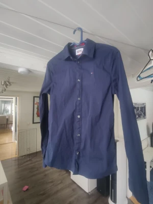 Mörkblå skjorta från Tommy Hilfiger/xs - Snygg mörkblå skjorta från Tommy Hilfiger med klassisk krage och knappar hela vägen. Liten logga på bröstet och långa ärmar med manschett. Perfekt för en stilren look.