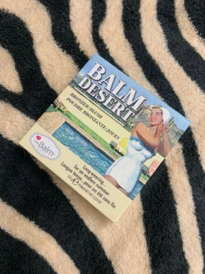 theBalm Balm Desert Bronzer/Blush - Snygg bronzer och blush från theBalm i nyansen Balm Desert. Kommer i en kompakt förpackning med retrodesign och spegel. Ger en naturlig solkysst look med en matt finish. Perfekt för att framhäva kindbenen och ge värme till ansiktet.