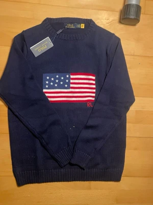 Marinblå stickad tröja Ralph Lauren - Snygg marinblå stickad tröja från Ralph Lauren med amerikansk flagga broderad på bröstet och RL-detalj i rött. Tröjan har rund halsringning och ribbade muddar vid ärmslut och nederkant. Perfekt för dig som gillar klassisk preppy stil. Såklart äkta ‼️ skriv vid minsta fundering