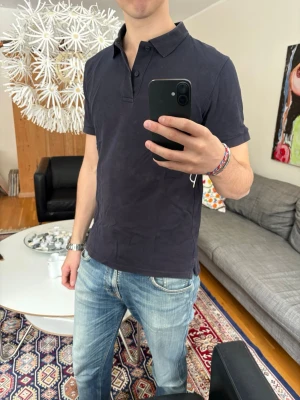 Mörkblå pikétröja med krage - Snygg mörkblå pikétröja med klassisk krage och korta ärmar. Tröjan har en stilren design utan synliga loggor och är tillverkad i mjuk bomull som känns skön mot huden. 