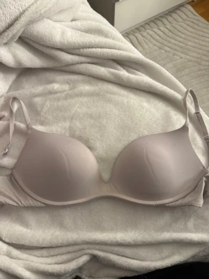 Vit  vadderad bh med bygel - Säljer en ljusrosa bh med vadderade kupor och bygel för extra stöd. Bh:n har släta kupor och justerbara axelband. Materialet känns mjukt och stretchigt, perfekt för en bekväm känsla under dagen.