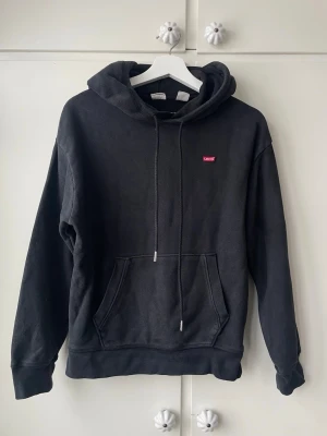 Svart hoodie från Levi's med logga - Svart Levi’s hoodie i storlek XXS. Använd men i fint skick.  Klassisk modell med luva och justerbara snören samt stor magficka framtill. Mjuk och bekväm passform, perfekt till vardags.  Snabb leverans. Skriv gärna vid frågor! 