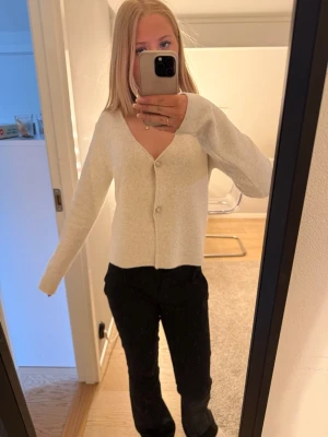 Ljusgrå cropped kofta med knappar - Snygg ljusgrå kofta med v-ringning och två knappar framtill. Modellen är cropped och har långa ärmar. Perfekt att styla med både jeans och kjol för en trendig look.