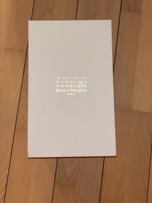 Maison Margiela Replica svarta sneakers - Maison Margiela Replica sneakers i svart mocka och läder med vita kontrasterande snören och vit insida. Klassisk låg modell med gummisula och stilren design. Perfekta för dig som gillar minimalistisk och exklusiv streetwear.   Ett par av de finaste skorna jag någonsin har sett. Hade verkligen inte viljat sälja dessa skorna men tyvärr så måste jag eftersom att storleken inte passar mig alls.  Rekommenderar dessa starkt!