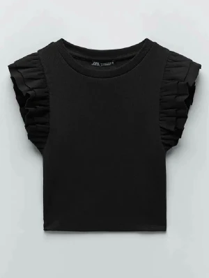 Svart topp med volangärmar från Zara - Stilren svart topp från Zara med korta volangärmar som ger en trendig touch. Toppen har rund halsringning och croppad passform. Perfekt att matcha med höga jeans eller kjol för en cool look. Denna är i st M och är helt oanvänd skulle säga att de passar vilken storlek som helst då den är stretchig. Min är helt oanvänd. 