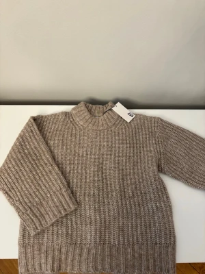 Beige stickad tröja från lager 157 - Säljer en chunky beige stickad tröja från lager 157 med hög krage och breda ribbade muddar. Tröjan har en avslappnad passform och är perfekt för lager på lager. Materialet känns mjukt och mysigt, perfekt för kyliga dagar.