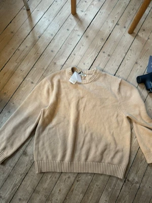 Beige stickad tröja från Soft Goat - Säljer en beige stickad tröja från Soft Goat i mjuk och lyxig kvalitet. Tröjan har rund halsringning, ribbstickade muddar och en avslappnad passform. Perfekt för dig som gillar stilrena och tidlösa plagg. Helt oanvänd med tag! Ull och Kashmirblandning