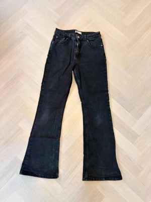 Svarta bootcut jeans med hög midja - Säljer ett par svarta bootcut jeans med medel midja och fickor. Jeansen har utsvängda ben och stängs med dragkedja och knapp. Perfekta för dig som gillar en retroinspirerad look och vill ha ett par bekväma jeans i stretchigt denim.