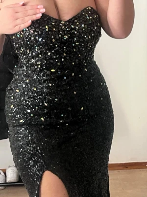 Svart glittrig långklänning - Supersnygg svart långklänning med massor av paljetter och glittriga detaljer. Axelbandslös modell med figurnära passform och hjärtformad urringning. Perfekt för bal eller festkvällar när du vill glänsa extra mycket.