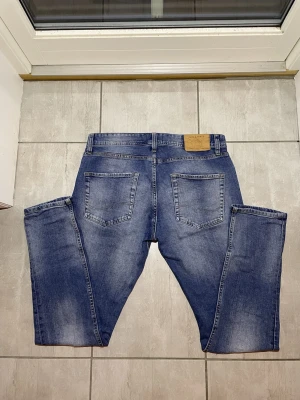 Blå Jack & Jones jeans slitningar  - Säljer ett par blå jeans från Jack & Jones med slitningar. Klassisk femficksmodell med knappgylf. Jeansen har två lite större hål och. Strl: 31,32. Vid frågor  och funderingar skriv gärna!