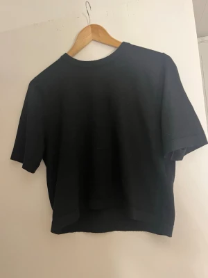 Stickad T-shirt  - En enkel svart finsstickad t-shirt med rund hals och korta ärmar. Perfekt till jeans eller kjol för en avslappnad look.