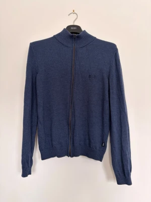 Hugo Boss Full Zip Merino Tröja – Strl S - Hugo Boss tröja med full zip i extrafine merinoull. Tunn, mjuk och exklusiv kvalitet som passar perfekt året runt. Storlek: S,  Färg: Blå,  Material: Extrafine merino wool,  Passform: Slim/regular,  Skick: Mycket bra,  Detaljer: Diskret Hugo Boss-logga på bröstet,   Stilren och tidlös – funkar lika bra till vardag som till mer uppklädda outfits.   Pris: 699 kr  Skickas snabbt, hör av dig vid frågor.