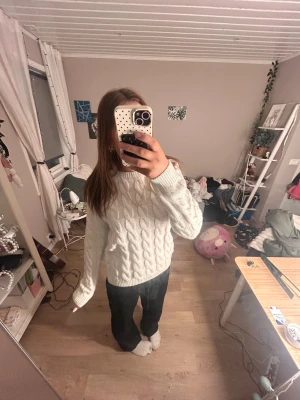 Vit kabelstickad tröja - Mysig vit kabelstickad tröja med rund hals och långa ärmar. Tröjan har ett klassiskt flätmönster och ribbade muddar vid ärmslut och nederkant. Perfekt för kalla dagar och enkel att matcha med olika outfits.