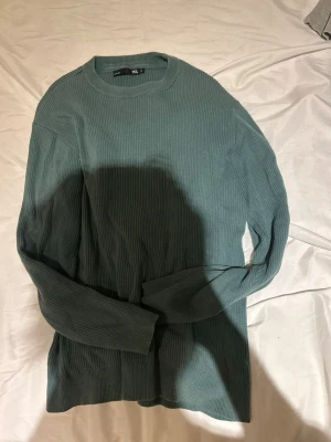 Grön ribbstickad tröja från 157 - Säljer en grön ribbstickad tröja från 157 med rund halsringning och långa ärmar. Tröjan har en enkel och stilren design, perfekt för lager på lager och passar till många olika outfits. Materialet känns mjukt och bekvämt.