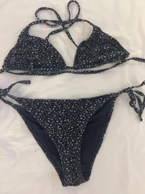 Mörkblå blommig bikini med knyt 💙🐠 - Söt mörkblå bikini med små blommor i vitt och ljusblått. Överdelen har trekantskupor och knyt i nacken och ryggen, medan underdelen har knyt i sidorna. Perfekt för stranden eller poolen! 🐠💙