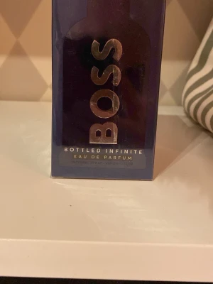 (Helt ny) BOSS Bottled Infinite Eau de Parfum - BOSS Bottled Infinite Eau de Parfum från Hugo Boss i en elegant mörkblå rektangulär förpackning med stora silverfärgade bokstäver. Parfymen har en modern och stilren design som passar perfekt för dig som gillar exklusiva dofter.