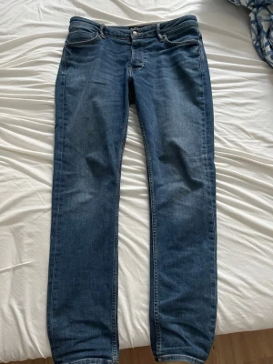 Neuw jeans slim fit - Säljer ett par blåa neuw jeans med slim passform. Jeansen har en klassisk blå denimfärg, silverfärgade knappar och kontrastsömmar. Materialet är bomullsdenim och de har bälteshällor samt en patch bak i midjan.