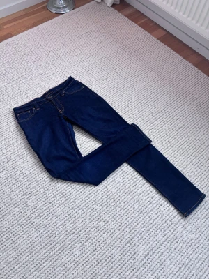 Mörkblå jeans från Nudie Jeans - Säljer ett par mörkblå jeans från Nudie Jeans med klassisk femficksmodell och kontrastsömmar. Slim jeans. Mycket fint skick. Storlek W30 L32. Skriv vid frågor
