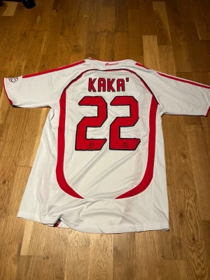 Milan 06 cl final Kaka #22 - Vit AC Milan matchtröja från Adidas med Kaka och nummer 22 på ryggen. Tröjan har röda och svarta detaljer, Champions League-märke och Bwin som sponsor på bröstet. Perfekt för fotbollsfans som vill sticka ut på läktaren eller planen.