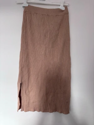Beige ribbad långkjol med slits - Säljer en beige ribbad långkjol med slits på sidan. Kjolen har en elastisk midja och är stickad i ett mjukt material som ger en skön passform. Perfekt för dig som gillar en enkel och stilren look.