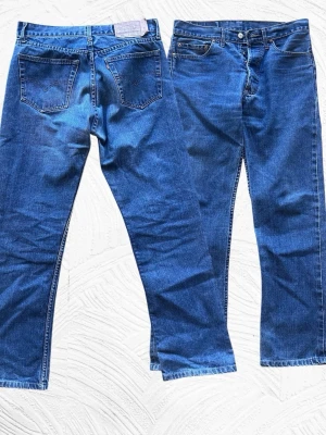 Levi's Jeans - Klassiska Levi's 501 jeans i blå denim med rak passform och fem fickor. Jeansen har knappgylf och tydliga sömmar, samt den ikoniska läderpatchen bak i midjan. Perfekta för en avslappnad och tidlös stil.