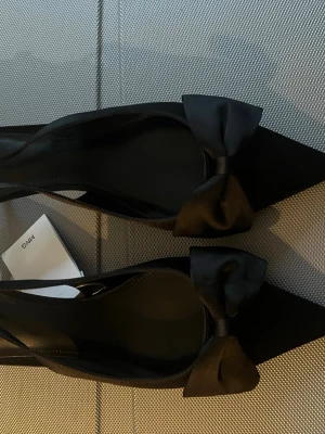 Svarta kitten heels med rosett från Mango - Stilrena svarta kitten heels med slingback från Mango med spetsig tå och dekorativ rosett framtill. Nyköpta - aldrig använda - med prislapp. 