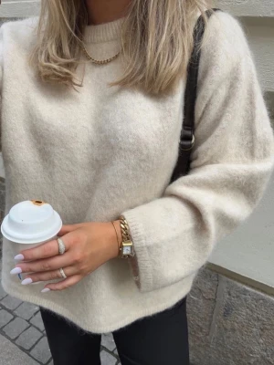 Beige oversized stickad tröja - Mysig oversized stickad tröja i beige med rund halsringning och långa ärmar. Tröjan har en fluffig, mjuk struktur och avslappnad passform. Perfekt att styla med jeans eller kjol för en chill look.