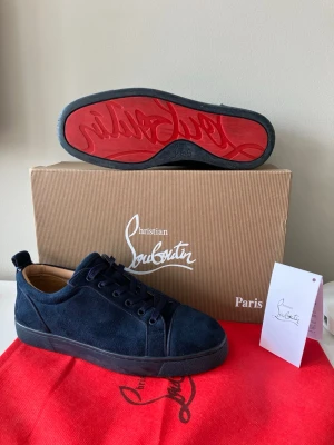 Mörkblå sneakers Christian Louboutin - Snygga mörkblå sneakers från Christian Louboutin i mocka med klassisk röd sula och svarta snören. Låg modell med rund tå och diskret logga på sulan. Perfekta för dig som vill ha något exklusivt. Jag tror att storleken på dem är trettioåtta men eftersom de är stora så passar det en storlek fyrtio. Skorna är väldigt sköna och jag har inte använt dem så mycket.